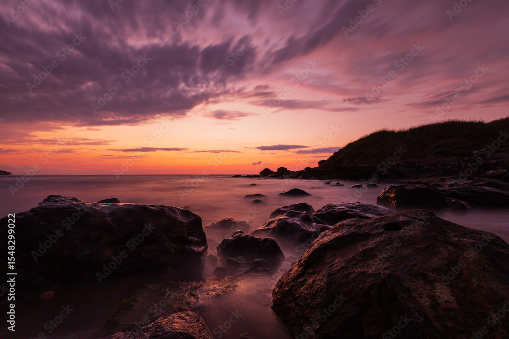 Fototapeta premium Rocky shore at sunset with long exposure sea and colorful clouds