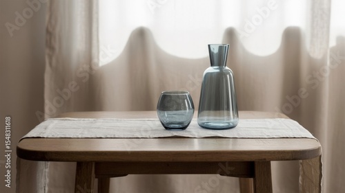 Elegant glass carafe and tumbler in soft blue hues on a wooden table with a linen runner - AI generated
