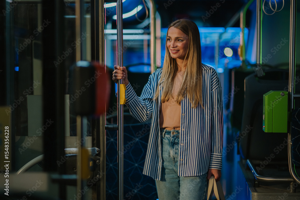 Fototapeta premium Young woman holding handrail while riding bus at night