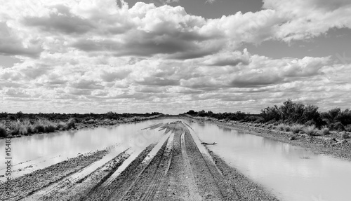 Imagem em preto e branco mostrando um trecho de estrada de rípio na Patagônia Argentina com grande extensão de água parada