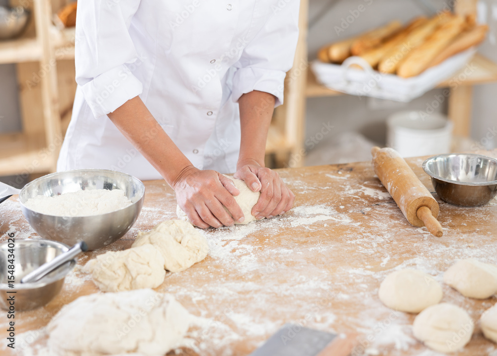 Fototapeta premium Cute doughs arranged on table in light bakery with close-up of woman's hands skillfully kneading dough at food production line