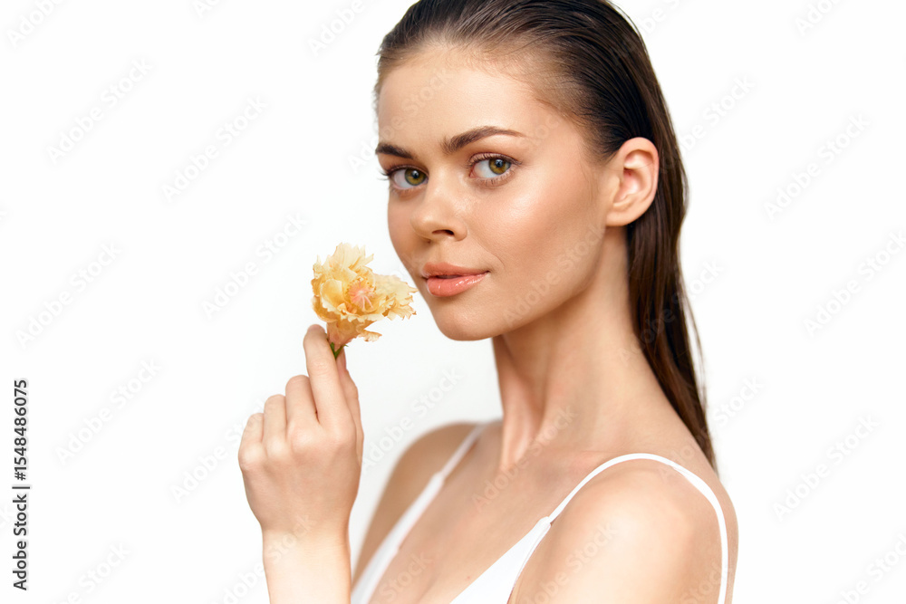 Beautiful female model holding a delicate flower with a gentle expression, featuring soft skin tones and a minimalistic background. Beautiful female model holding a delicate flower with a gentle expression, featuring soft skin tones and a minimalistic background.
