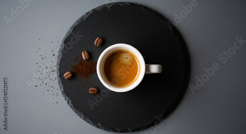 Aerial shot of espresso in white cup on black slate with coffee beans and grounds scattered around it