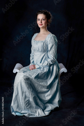 A Regency woman wearing a blue cotton dress and sitting on a wooden seat