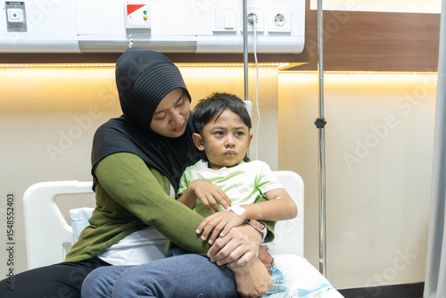 Asian muslim mother hug her son in hospital bedroom; mother caring her child when he is sick