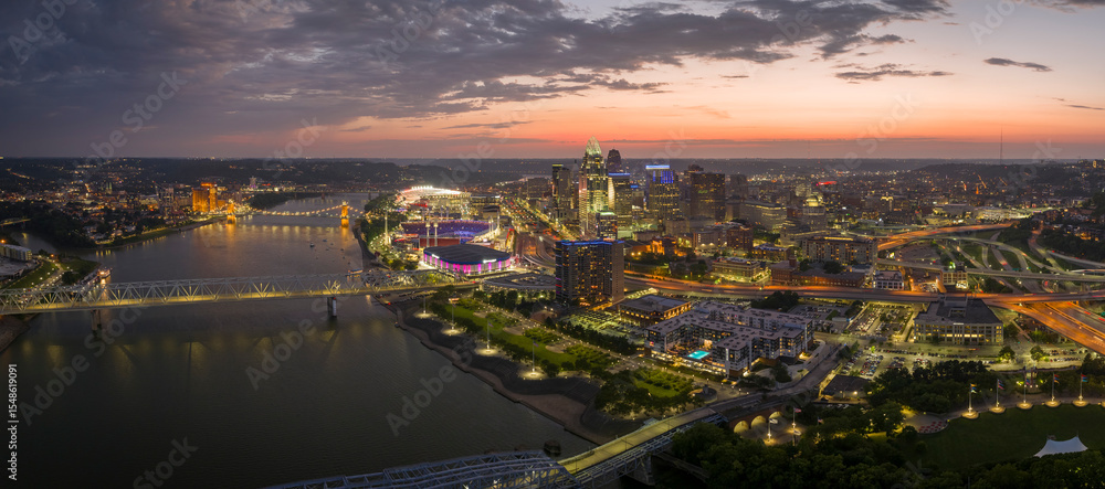 Fototapeta premium Cincinnati city, Ohio, USA with bridge highway traffic driving cars in downtown district. American city skyline with brightly illuminated high commercial buildings at night