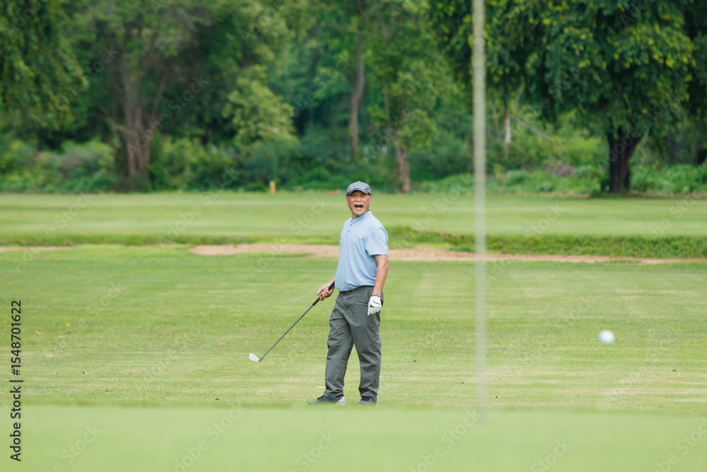 Fototapeta premium Elderly Asian man enjoying the morning round of golf in soft and warm sunlight.