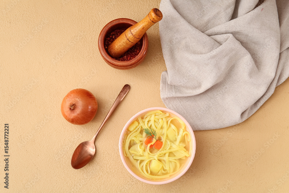 Fototapeta premium Bowl of tasty chicken soup, onion, mortar and pestle on beige background