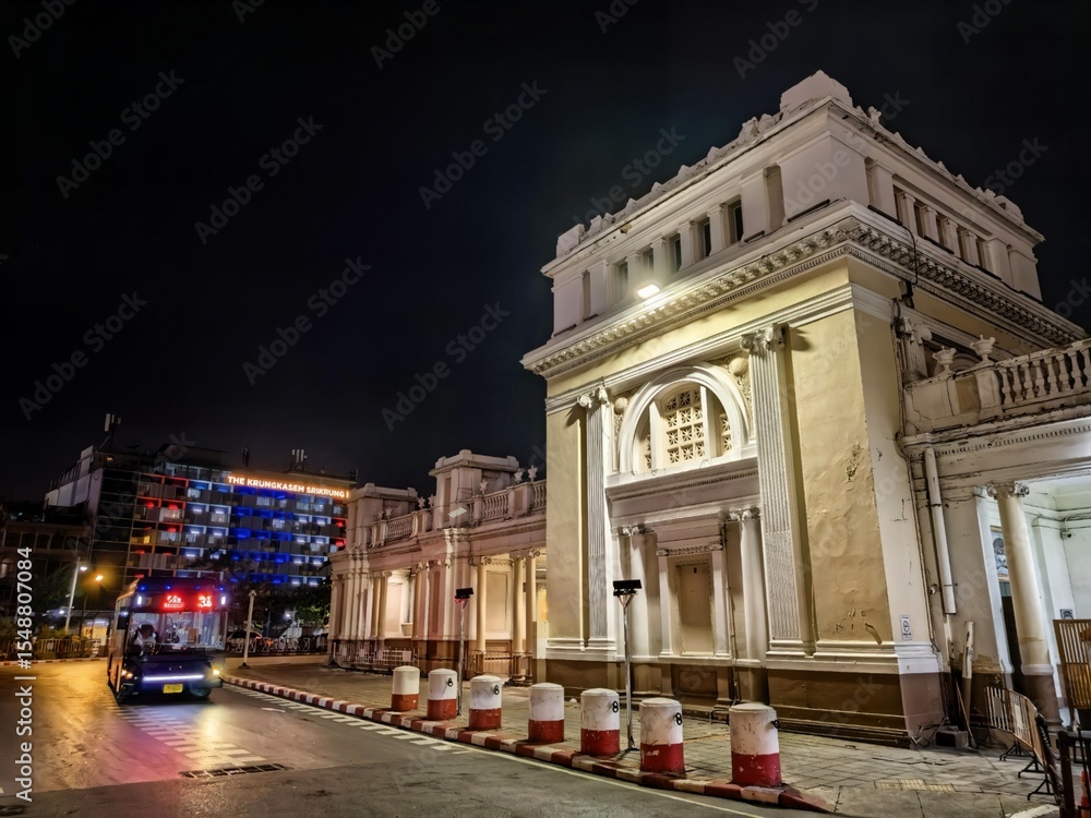 Fototapeta premium Grand historic building at night with a bus passing by in Bangkok