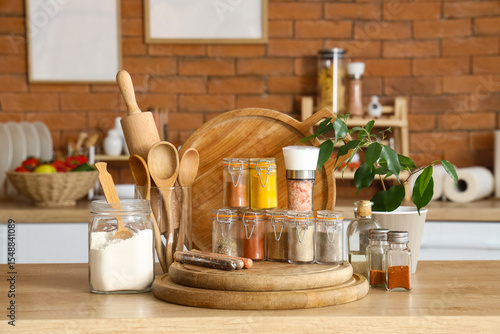 Fototapeta Naklejka Na Ścianę i Meble -  Jars with different spices, utensils and plant on table in kitchen