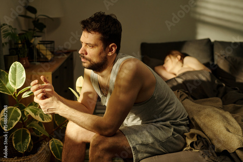 Foto Man sitting on bed looking away with thoughtful expression while woman lying in