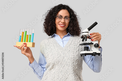 Female African-American teacher with microscope and test tubes on light backg...