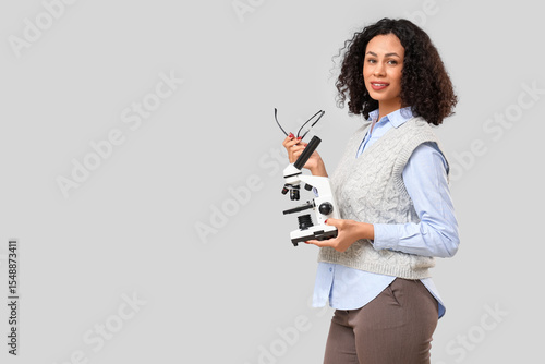 Female African-American teacher with microscope and eyeglasses on light backg...