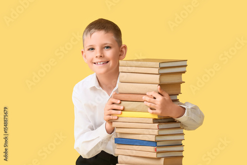 Smiling little boy with stack of books against color background