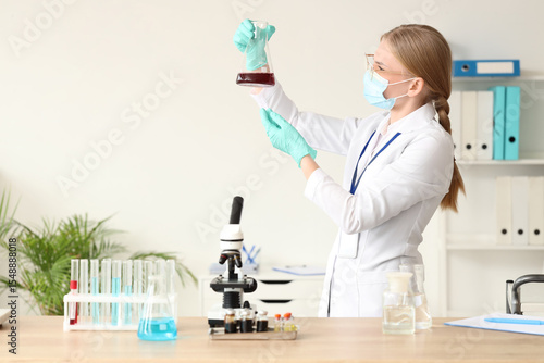 Female scientist with flask and microscope on table in laboratory