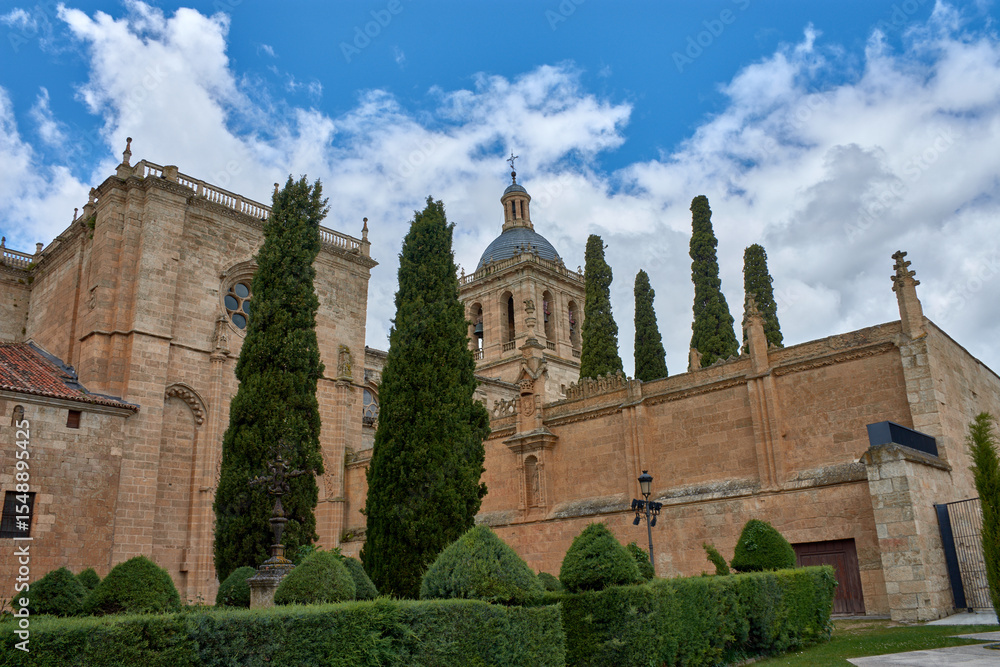 Fototapeta premium Detailed view of the Romanesque tower of Ciudad Rodrigo Cathedral in Salamanca, with a cloudy sky and green trees in the foreground