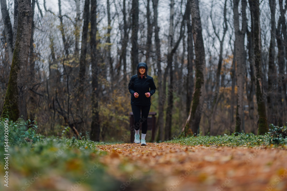 Fototapeta premium Woman jogging on a trail in the woods during autumn