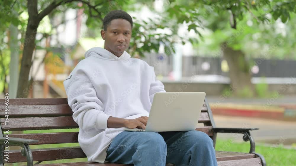 Casual African American Man Giving Thumbs Down with Laptop Outdoors Casual African American Man Giving Thumbs Down with Laptop Outdoors