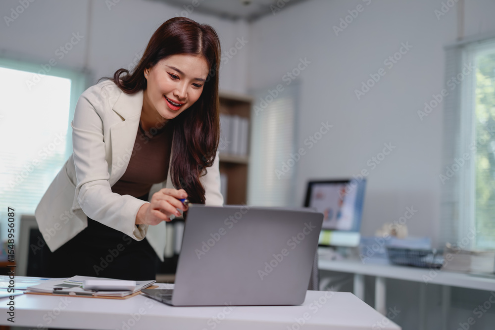 Young businesswoman pointing at her laptop screen while working at a bright, modern office desk, demonstrating engagement with her tasks and technology Young businesswoman pointing at her laptop screen while working at a bright, modern office desk, demonstrating engagement with her tasks and technology