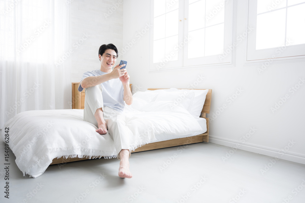 Whole body of thinking fresh man with smartphone relaxing on bed Copy space available Whole body of thinking fresh man with smartphone relaxing on bed Copy space available