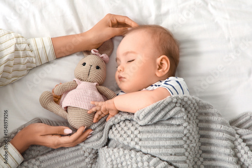 Fotografie Female hands and little baby with toy bunny sleeping on bed, top view
