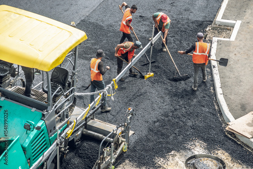 Workers lay a new asphalt coating using hot bitumen. Work of heavy machinery and paver. Top view