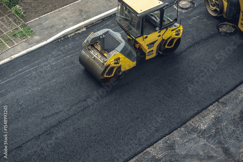 Workers lay a new asphalt coating using hot bitumen. Work of heavy machinery and paver. Top view