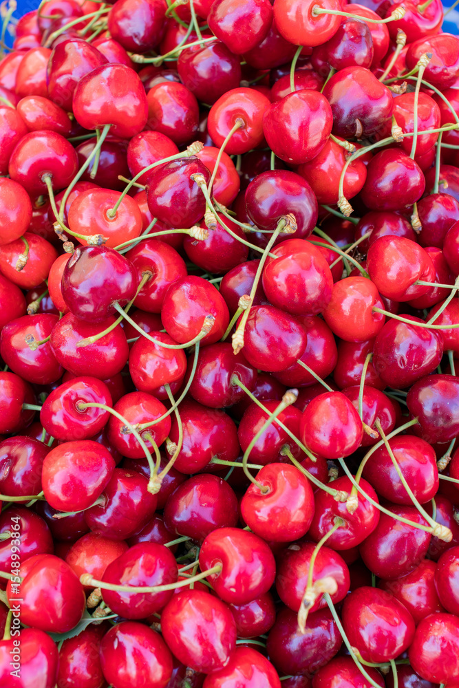Close-up of a pile of fresh ripe red cherries with stems. Healthy organic fruit on sale at a local market. Bright and colorful food background. Close-up of a pile of fresh ripe red cherries with stems. Healthy organic fruit on sale at a local market. Bright and colorful food background.