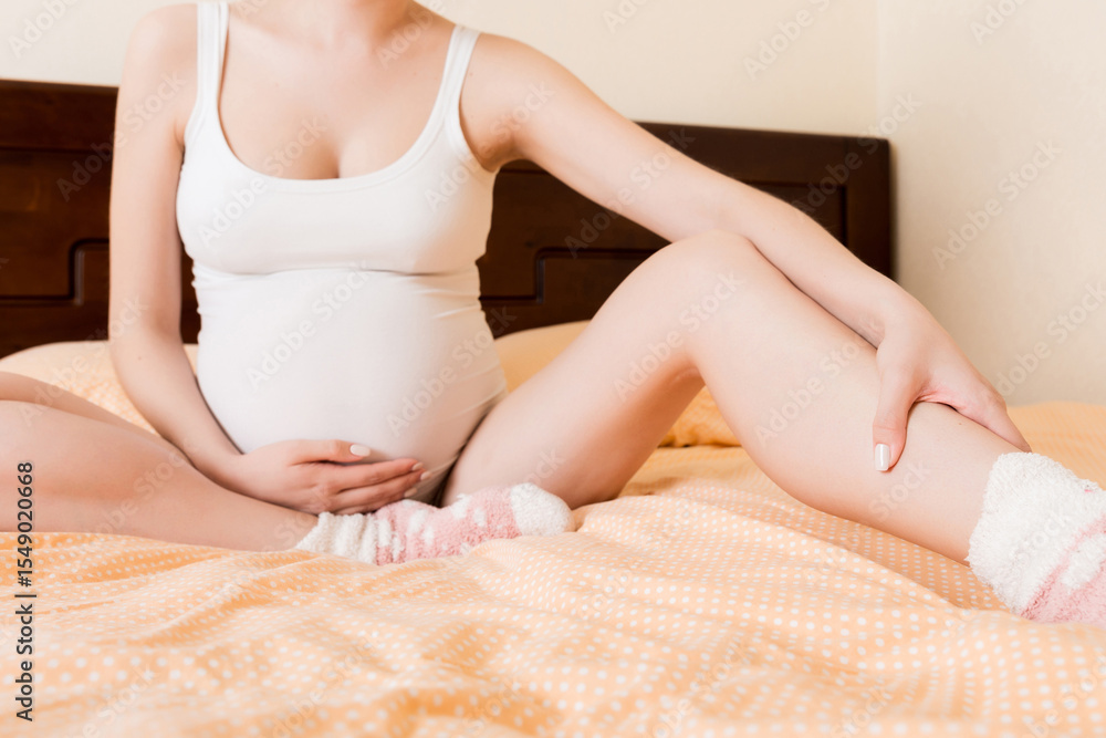 Fototapeta premium Pretty pregnant woman hands massaging leg sitting on bed