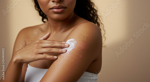 Young woman applying cream to her shoulder in soft lighting  