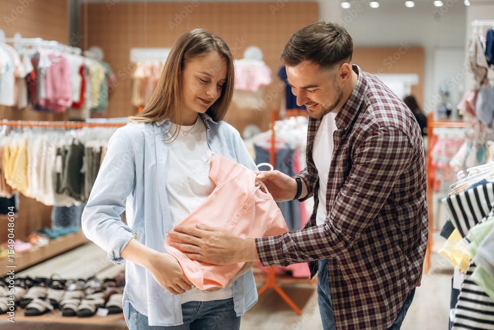 Obraz premium Wellbeing, choosing wear. Pregnant woman with man are in the kid's clothing store