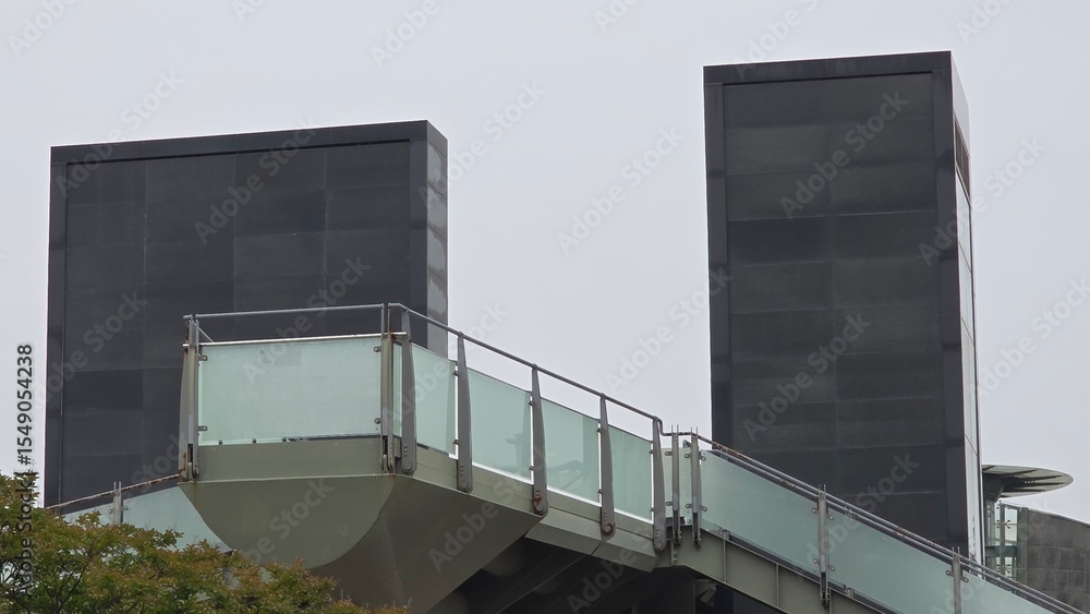 Fototapeta premium Two tall rectangular towers connected by a raised pedestrian walkway with frosted glass railing.