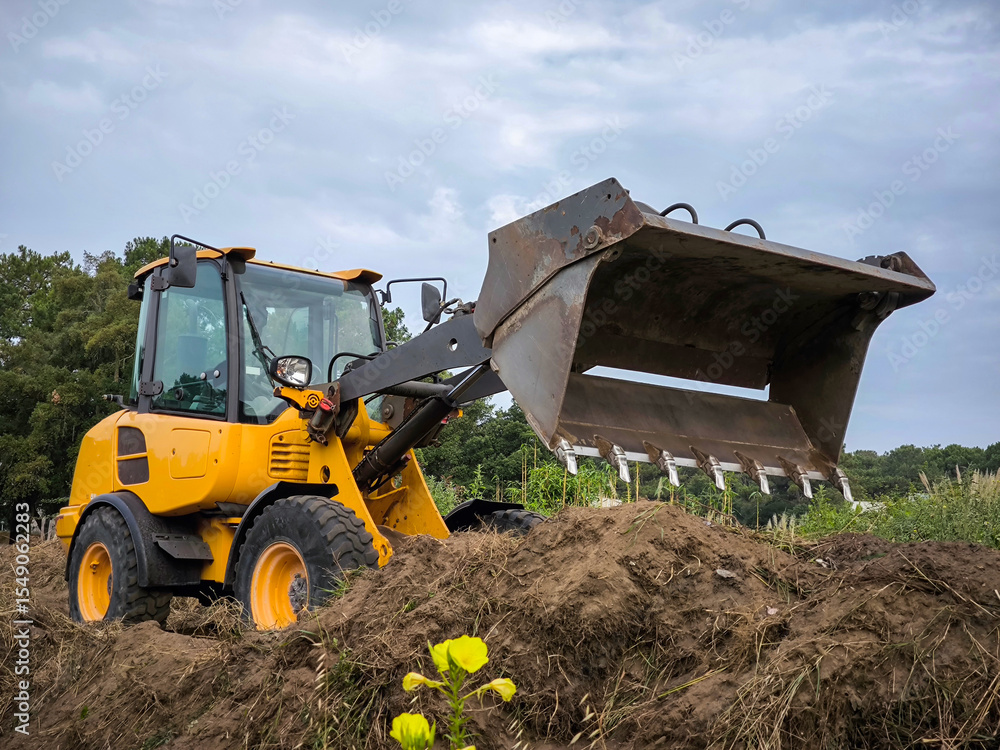 Obraz premium Carregadeira de rodas a trabalhar no espalhamento de terra em meio a uma fazenda agrícola para a construção de um caminho num dia nublado