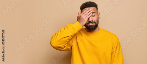Frustrated man in yellow shirt holding hand to forehead, expression of mistake, regret, or realization on beige background regret expression, forgot something, oops moment, human e