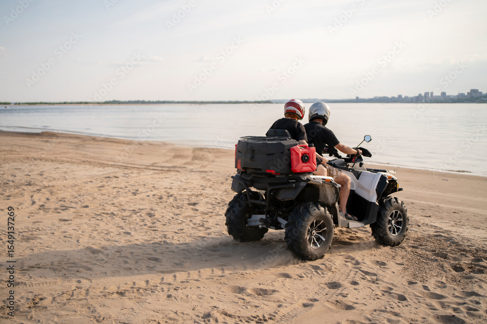 Obraz premium Exploring the sandy beach on an ATV during a calm afternoon with distant cityscape views