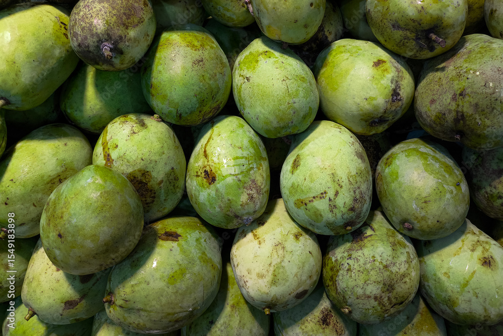A heap of fresh green mangoes with natural blemishes and moisture glistening under the market light. Tropical fruit display in a traditional market, perfect for healthy lifestyle themes. A heap of fresh green mangoes with natural blemishes and moisture glistening under the market light. Tropical fruit display in a traditional market, perfect for healthy lifestyle themes.