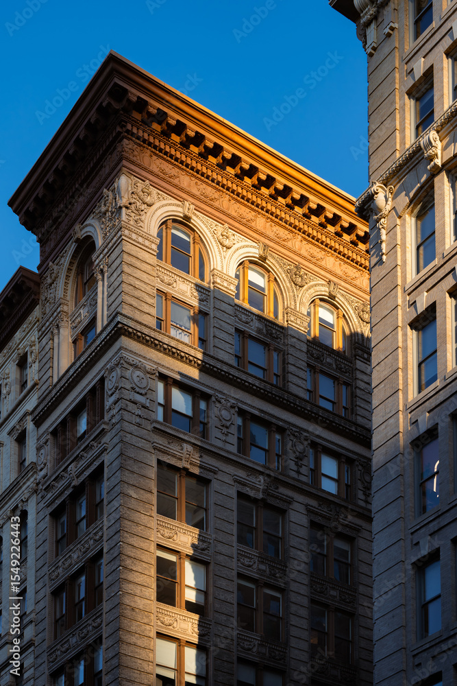 Obraz premium Last rays of sun on Soho loft building with facade ornamentation and copper cornice. Soho Cast Iron Building Historic District along Broadway, Lower Manhattan, New York City