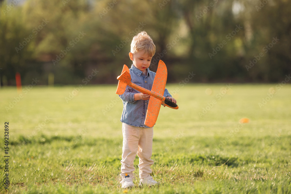Fototapeta premium Orange colored toy plane is in hand. Little boy is having fun on the field outdoors