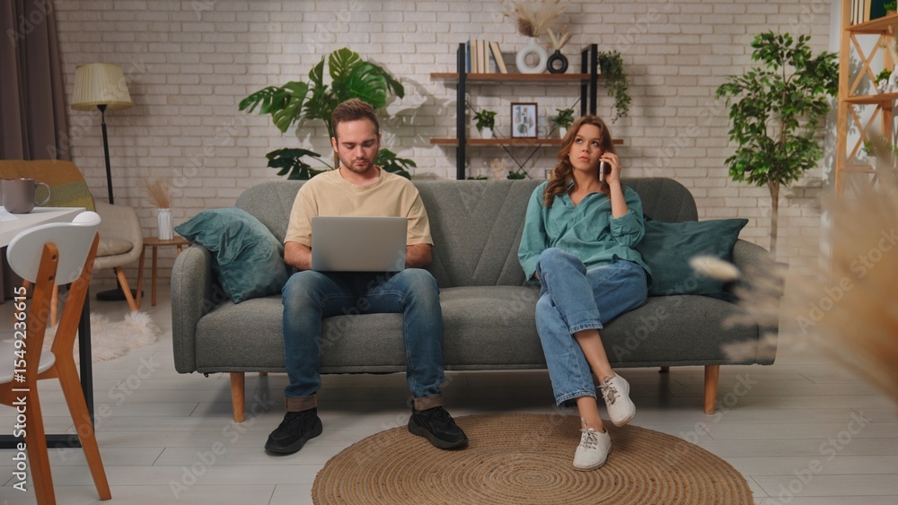 Obraz premium Young Couple Using Laptop and Phone on Modern Gray Couch
