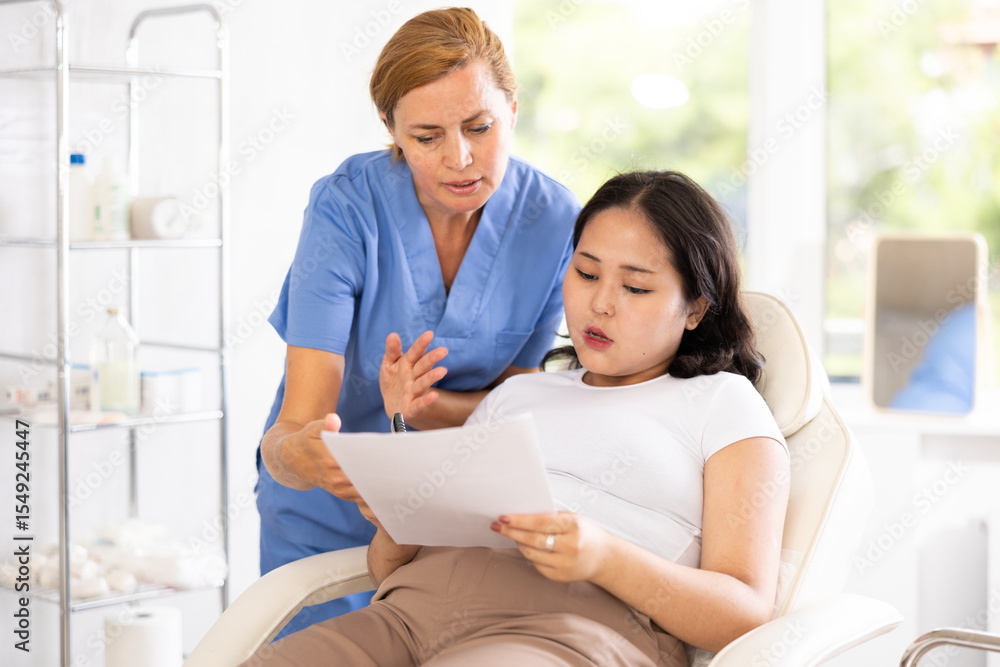 Obraz premium European doctor registering asian woman to cosmetology procedures in medical chair
