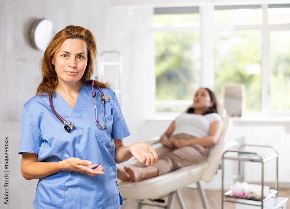 Obraz premium Smiling woman beautician wearing blue overall posing in clinic of esthetic medicine