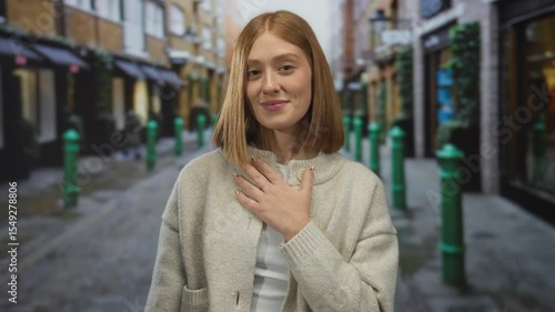 Wallpaper Mural Young blonde woman with bare arm places hand on chest in cobblestone city street; gratitude sincerity appreciation warmth. Torontodigital.ca