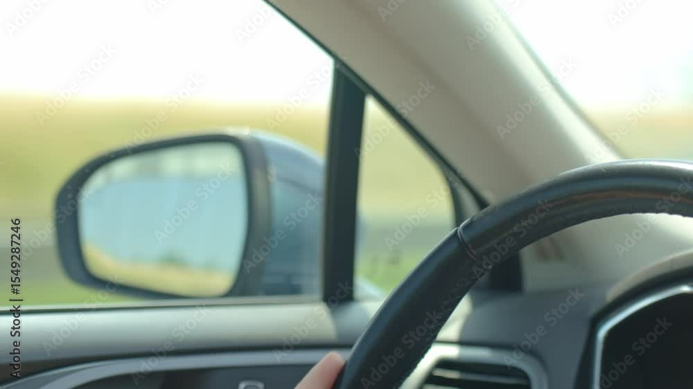 Close-up of hand on car steering wheel with road reflected in rear mirror. Male driver driving car, inside view Close-up of hand on car steering wheel with road reflected in rear mirror. Male driver driving car, inside view