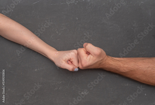 Slika na platnu Male and female fists pressing against each other on neutral gray background, creating tension through opposing forces
