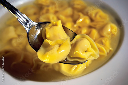 Spoon lifting tortellini from a bowl of broth