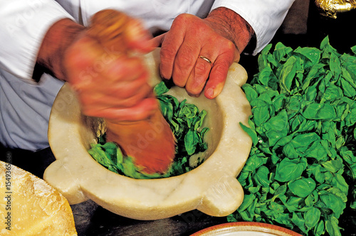 Chef crushing basil leaves with pestle in marble mortar