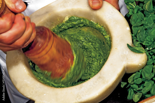 Chef preparing pesto with mortar and pestle, adding basil leaves