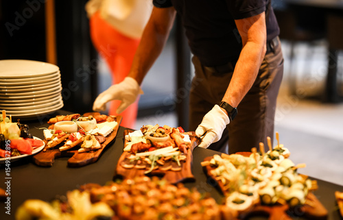 Caterer in white gloves arranging gourmet appetizer boards with cheeses, meats, and vegetables for an upscale event or celebration.