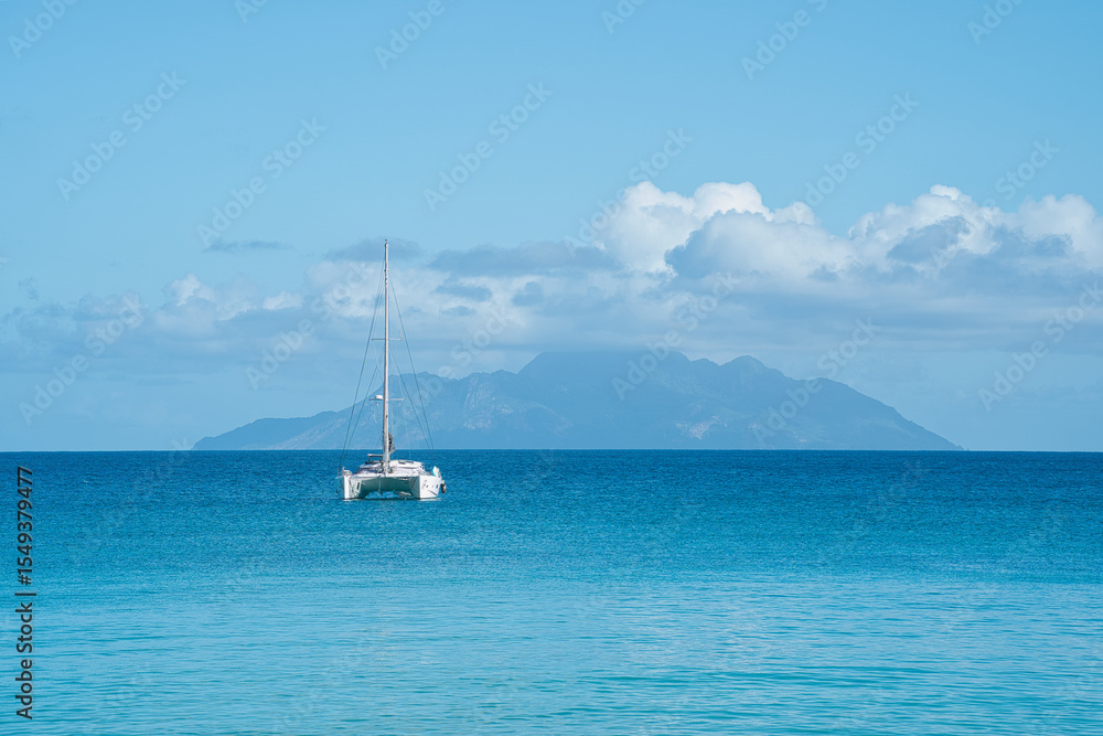 Fototapeta premium Beautiful beach of Beau Vallon, docking yacht, transparent and turquoise water, with silhouette island at the back, Mahe, Seychelles 