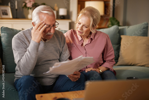 Fotografie An older Caucasian couple sits on their blue sofa while reviewing financial paperwork and insurance information